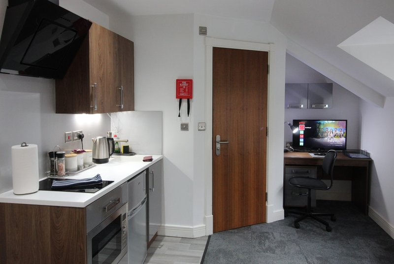 Modern kitchenette with brown cabinetry, white countertop, and integrated appliances in open-plan studio
