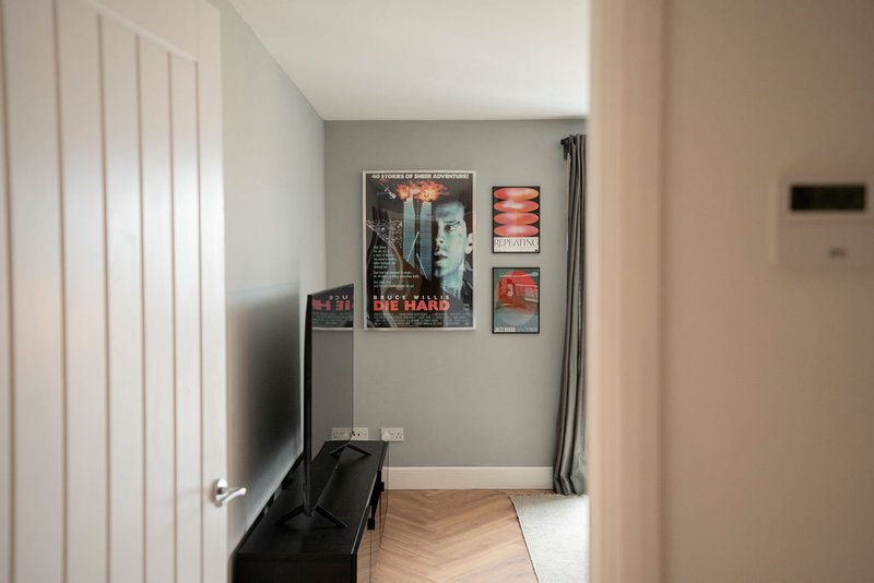 Bedroom entrance with white door, wall art prints, wooden floor and black luggage.