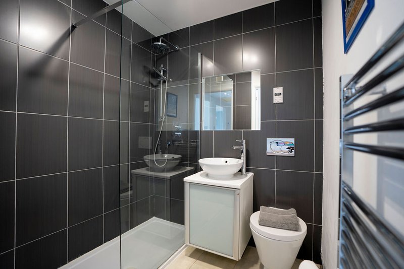 Modern bathroom with black tile walls, white vessel sink, toilet, and glass shower enclosure