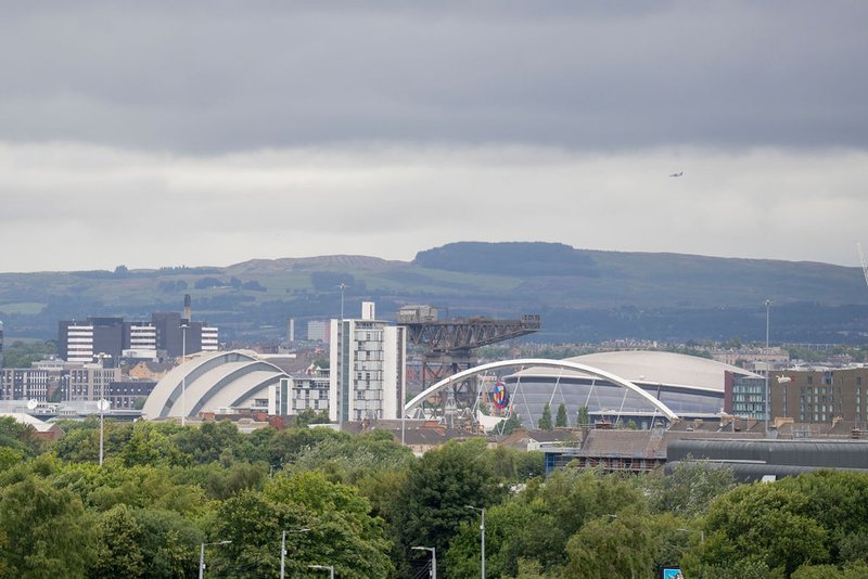 Urban skyline with modern buildings, curved architecture structures and green hills in background