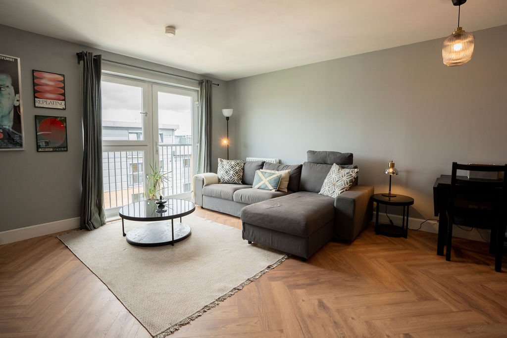 Modern living room with gray sectional sofa, wooden floor, area rug, and balcony access