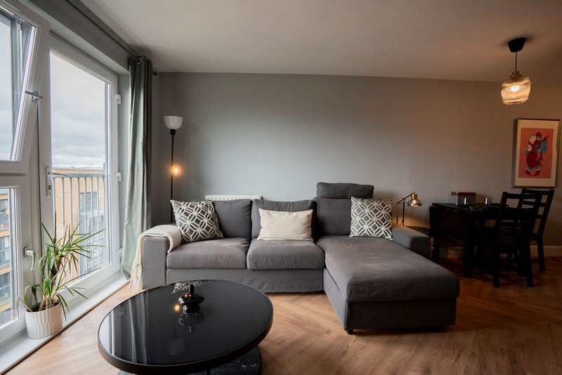 Modern living room with gray sectional sofa, black coffee table, and balcony doors overlooking city