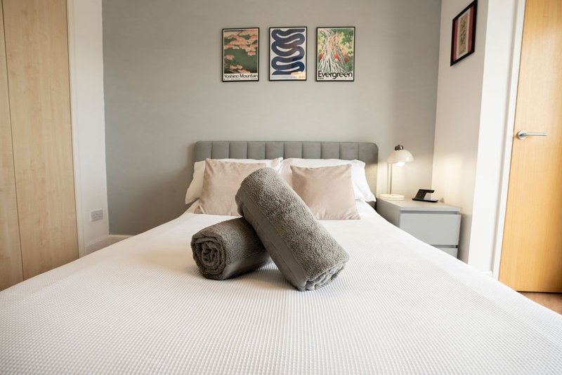 Modern bedroom with gray upholstered bed, white bedding, decorative pillows and wall art