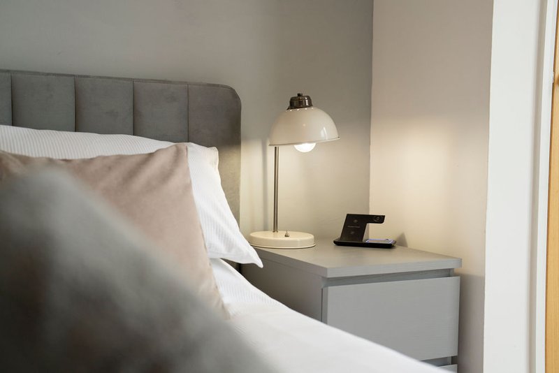 Modern bedroom with gray upholstered headboard, white bedding, and bedside table with lamp
