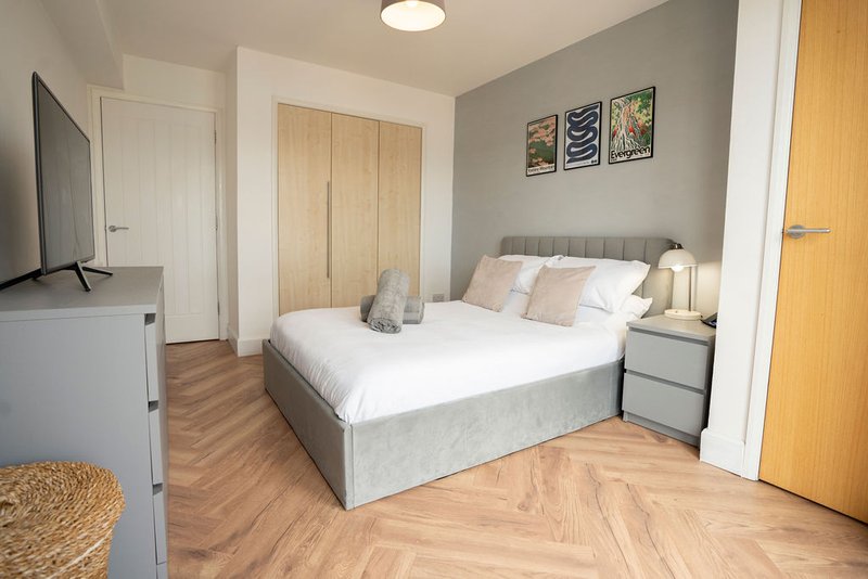 Modern bedroom with gray upholstered bed, wooden wardrobe, bedside table, and herringbone flooring