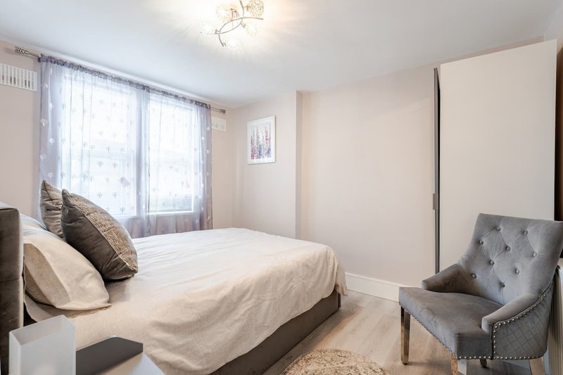 Bright bedroom with double bed, grey armchair, large windows and cream bedding