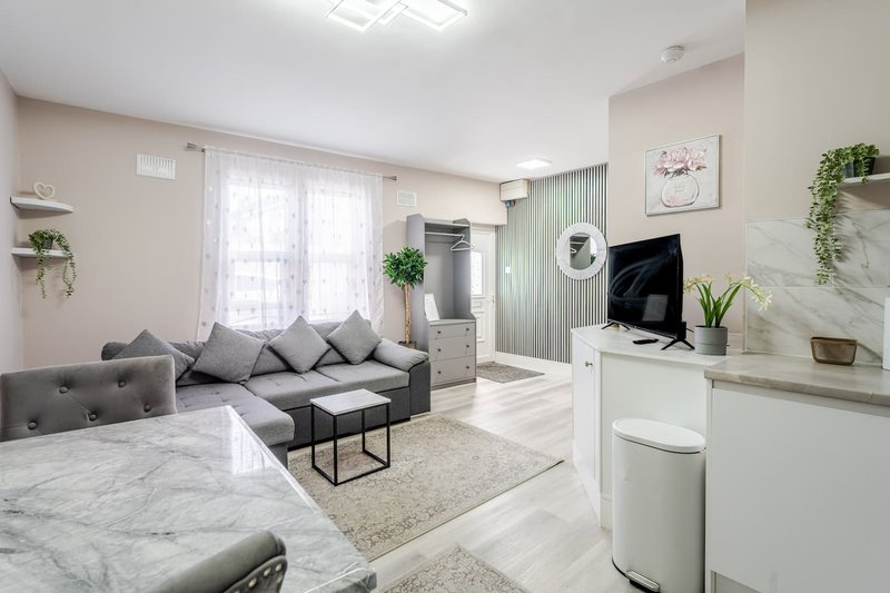 Modern open-plan living room with gray sofa, marble flooring, kitchenette and natural lighting