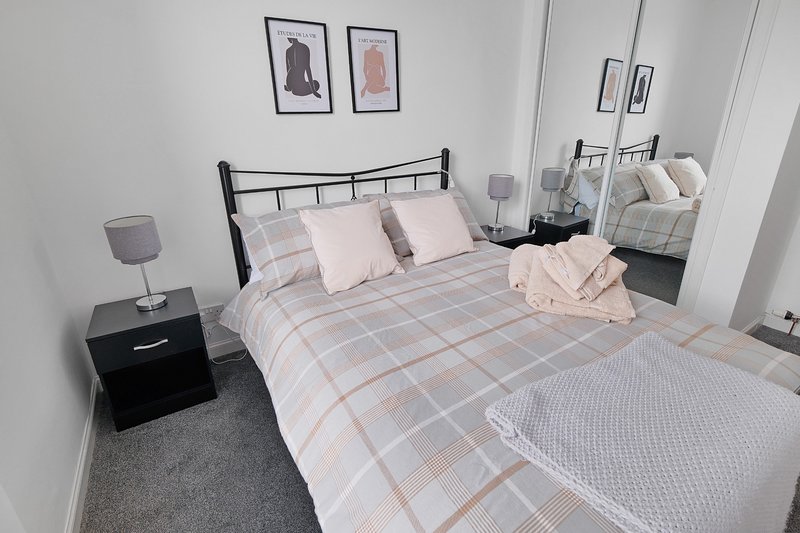 Modern bedroom with double bed, metal frame, pink and grey bedding, black nightstand, and wall art