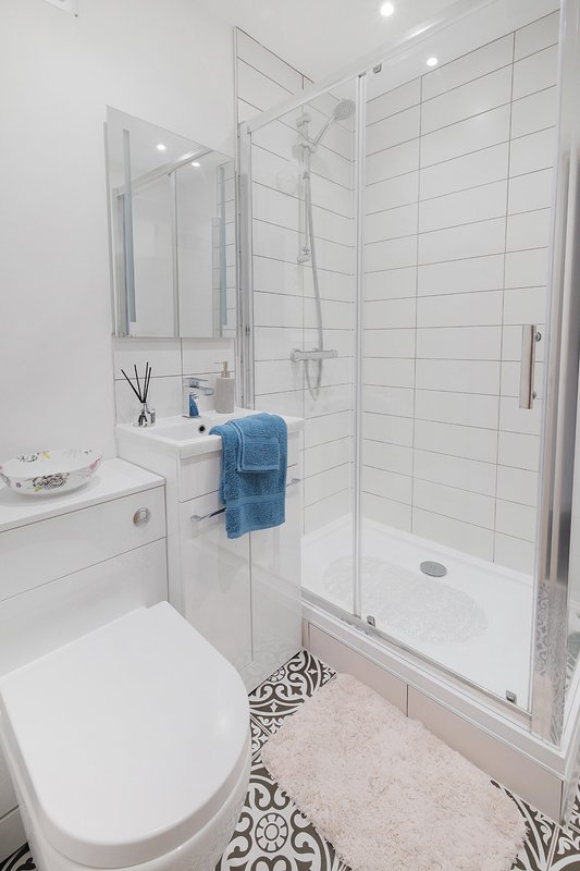 Modern bathroom with white subway tile shower, white vanity, toilet, and patterned floor tiles