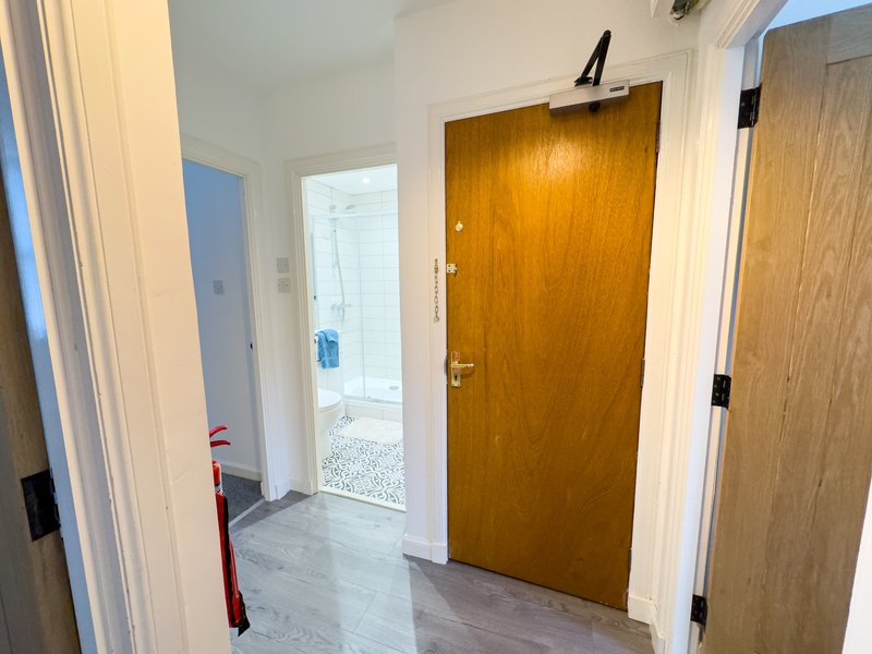 Hallway with wooden doors, white walls, and access to bathroom and kitchen areas