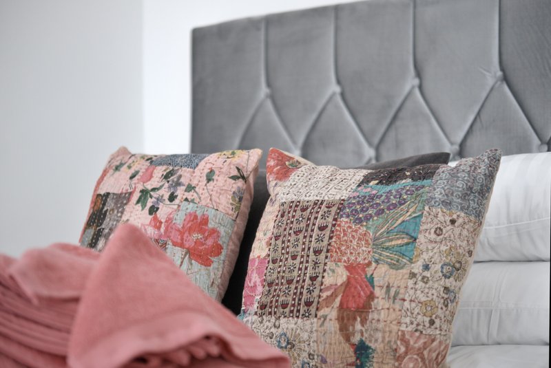 Bedroom with gray upholstered headboard, decorative patterned cushions and pink bedding