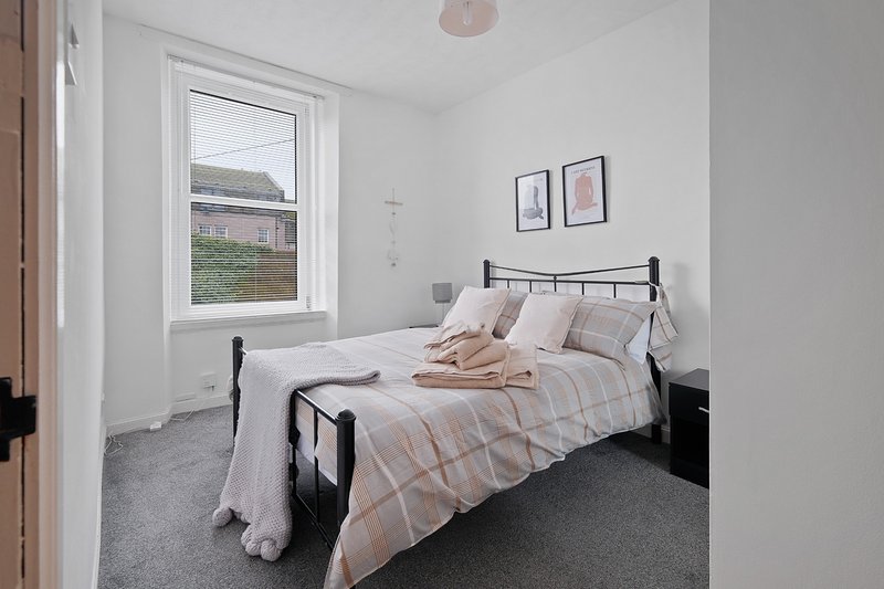 Bright bedroom with double bed, metal frame, striped bedding, window view, and wall art