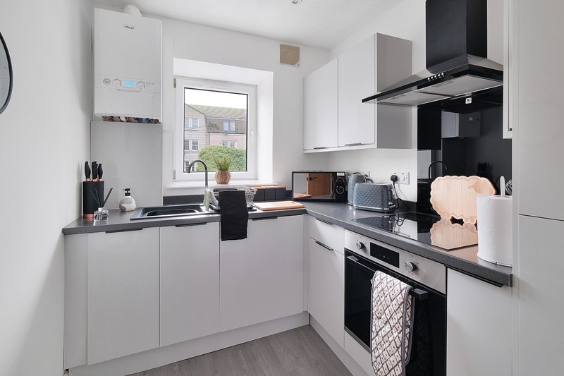 Modern white kitchen with black accents, stainless steel appliances, and window view