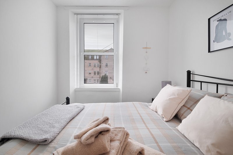 Bright modern bedroom with double bed, white walls, window view and framed wall art
