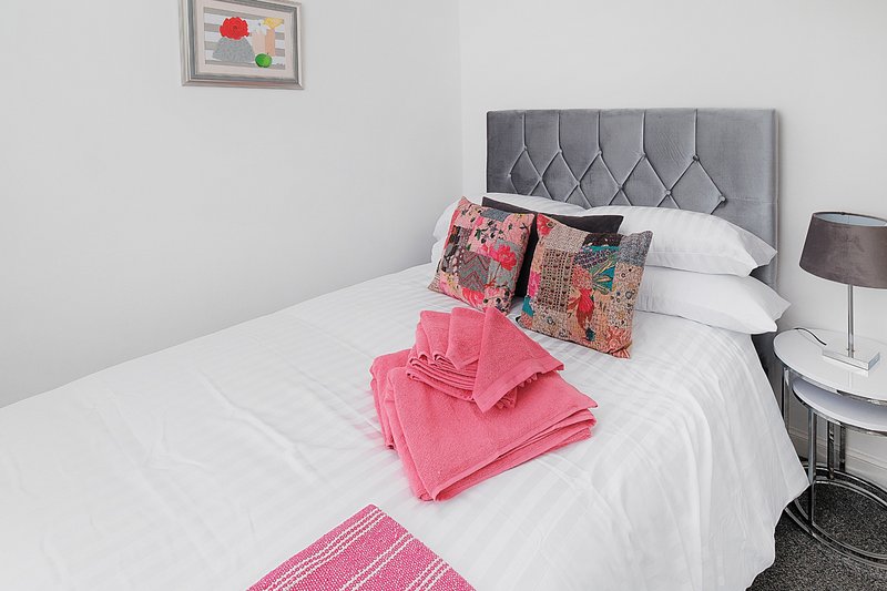 Modern bedroom with gray upholstered headboard, white bedding, pink cushions and towels