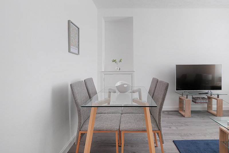 Modern dining area with glass table, gray chairs and TV mounted on wall