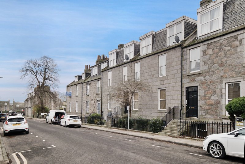 Street view of stone-built terraced houses with parked cars and bare tree