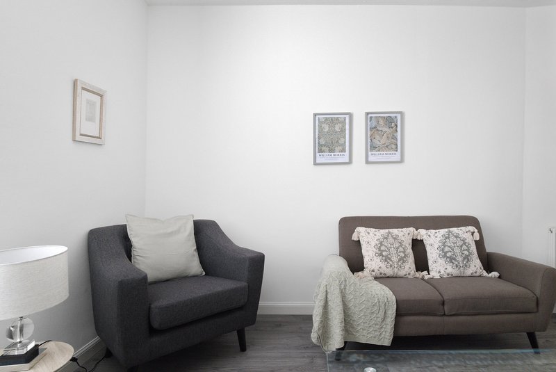 Modern living room with dark armchair, brown sofa, throw blanket, and framed artwork on white walls