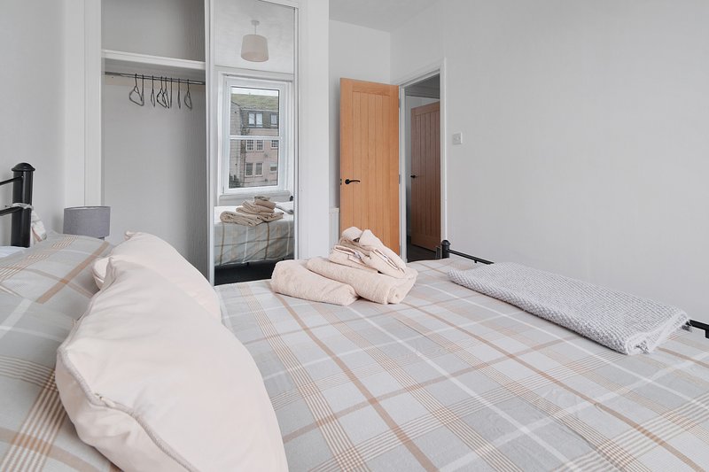 Bright bedroom with double bed, plaid bedding, wardrobe, and ensuite bathroom door
