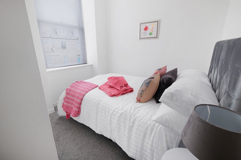 Bright bedroom with single bed, white bedding, pink throw, and small framed artwork