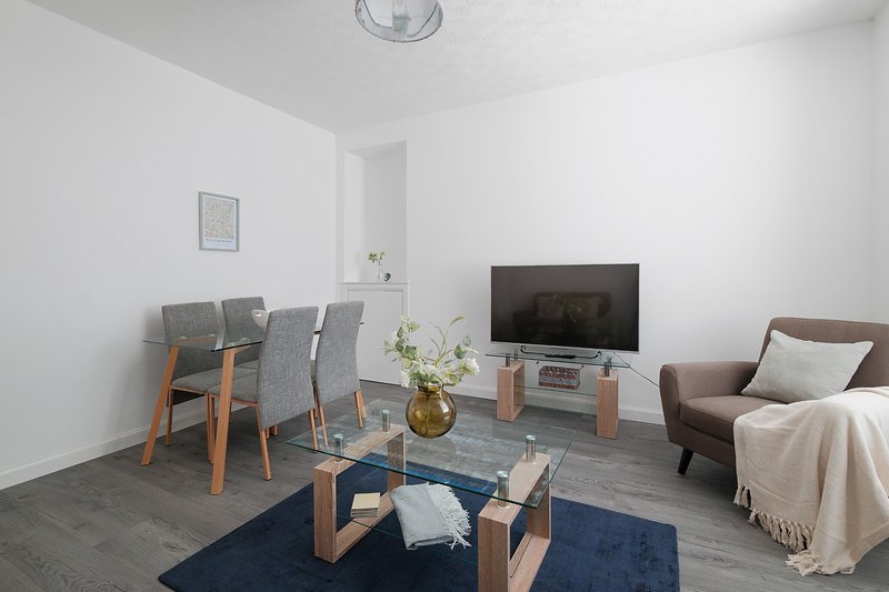 Modern living room with dining table, TV, sofa, and wooden furniture on grey flooring