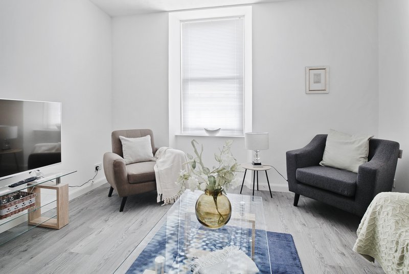 Bright living room with two armchairs, sofa, wooden floor, and large window