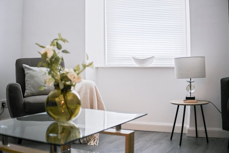 Modern living room with grey armchair, side table lamp, vase with foliage, and window