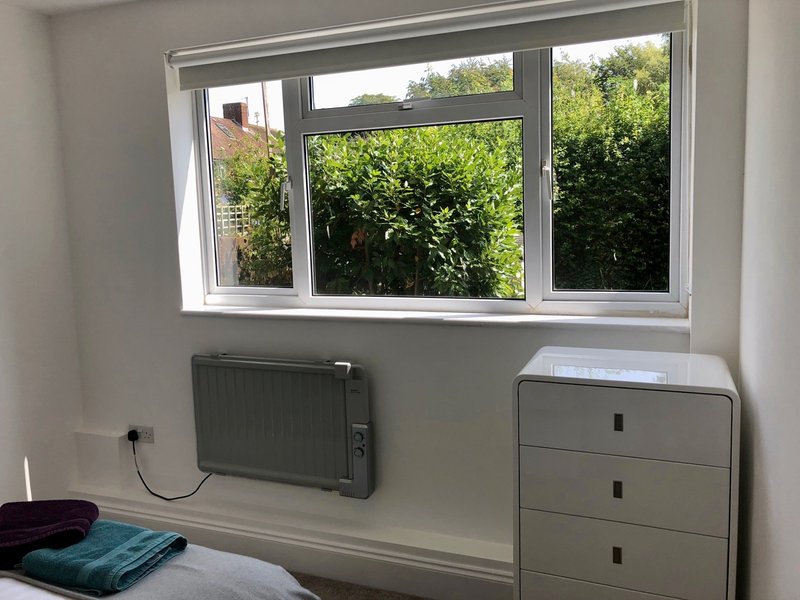 Bedroom with window overlooking garden, radiator, chest of drawers and folded textiles