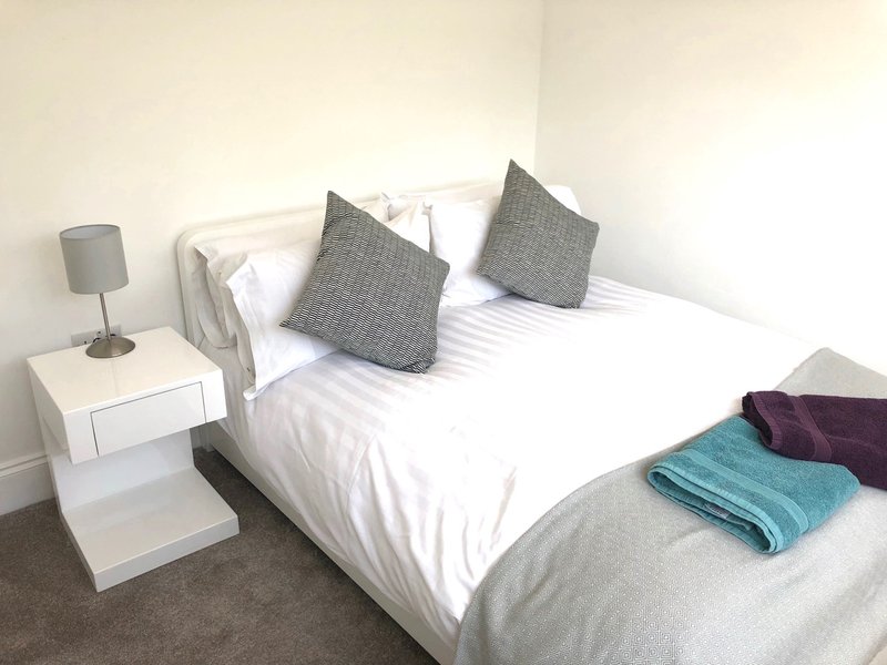 Modern bedroom with double bed, grey cushions, white bedding, and bedside lamp