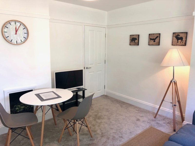 Modern home office with round white table, desk chair, monitor, tripod lamp and wall clock