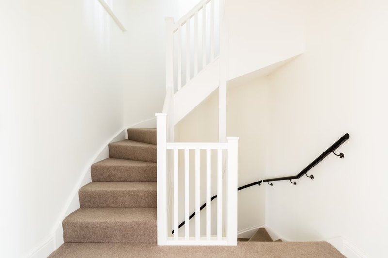Staircase with beige carpet, white railings and modern black handrail in bright interior