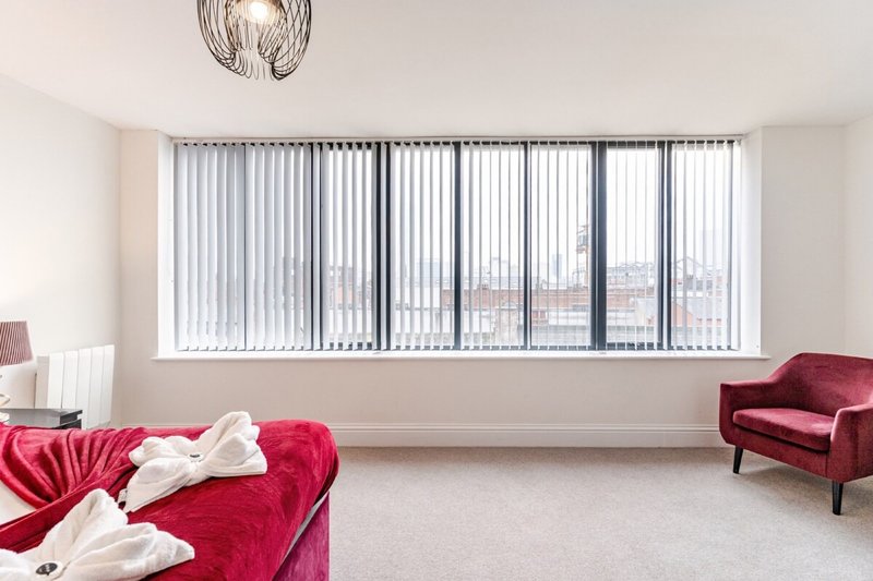 Bright modern living room with red velvet seating, vertical blinds, and city view from large windows