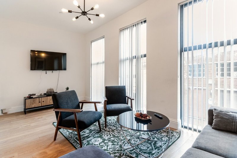 Modern living room with blue armchairs, round table, wall-mounted TV and large windows
