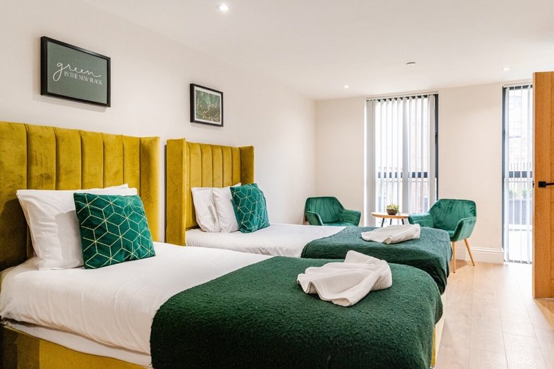 Bright twin bedroom with yellow upholstered headboards, white bedding, green accents and seating area