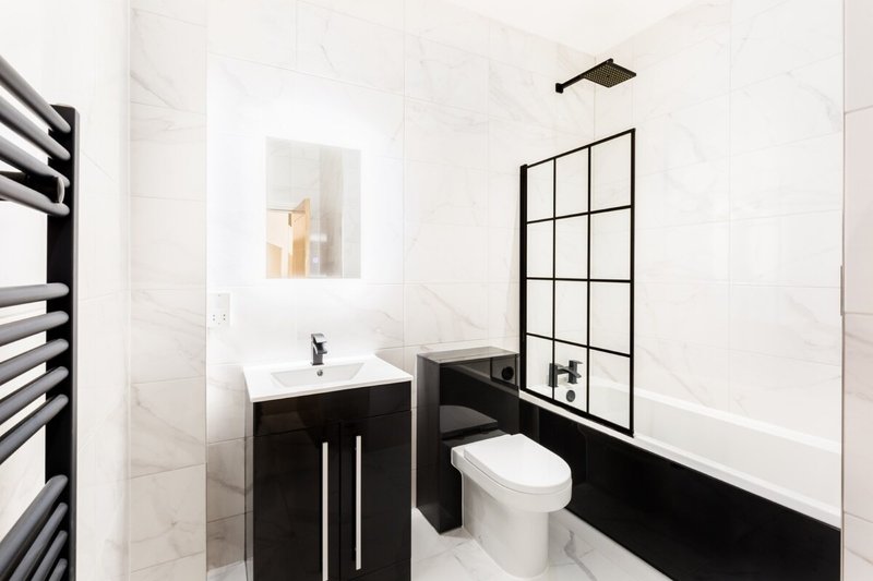 Modern bathroom with black vanity, white sink, toilet, and geometric shower screen