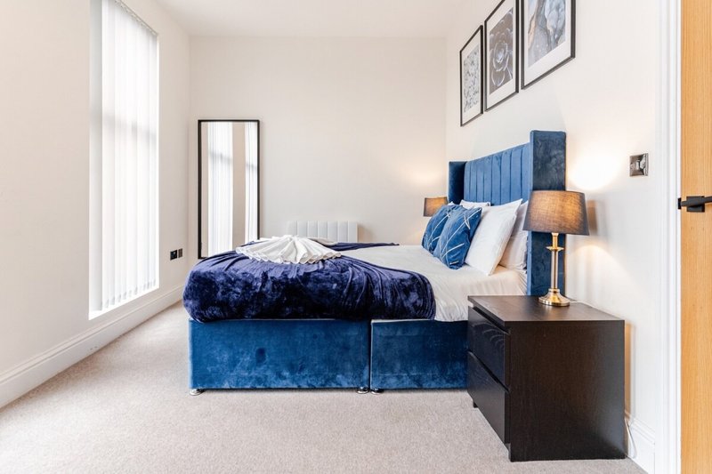 Modern bedroom with blue velvet bed, white bedding, dark nightstand and framed wall art