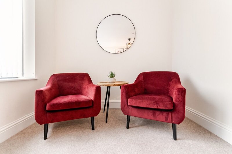 Two red velvet armchairs facing each other with small side table and round mirror