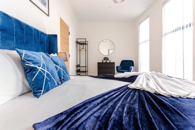 Bright bedroom with blue upholstered headboard, white bedding, navy throw, and modern furnishings