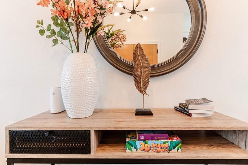 Wooden console table with white vase, dried flowers, round mirror, and decorative items
