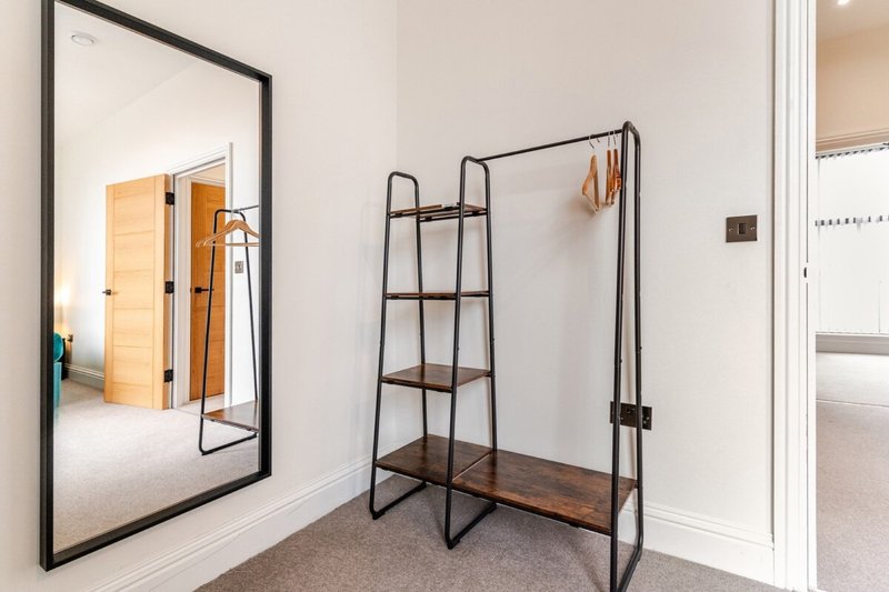 Modern bedroom corner with mirror, wooden clothing rack, and carpeted floor