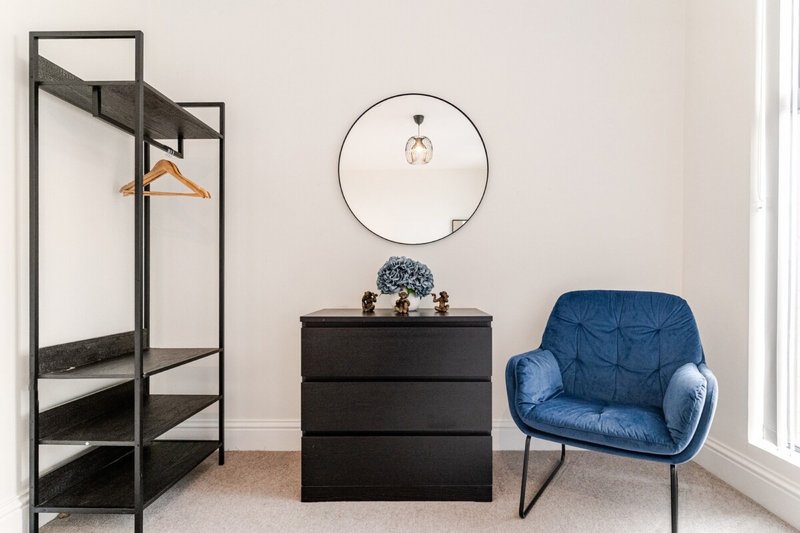 Bedroom corner with black metal frame bed, blue armchair, black dresser and circular mirror