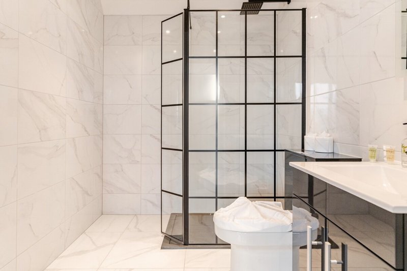 Modern bathroom with marble tiles, black-framed glass shower enclosure and white sink vanity