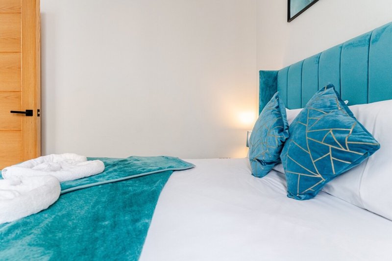 Modern bedroom with white bed, teal headboard, decorative pillows and wooden door