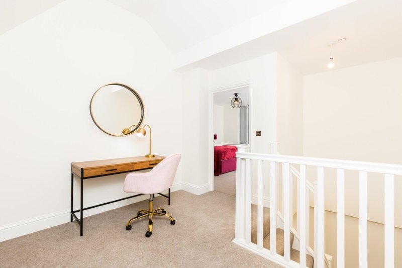 Modern bedroom with desk, chair, round mirror and white crib against pale walls