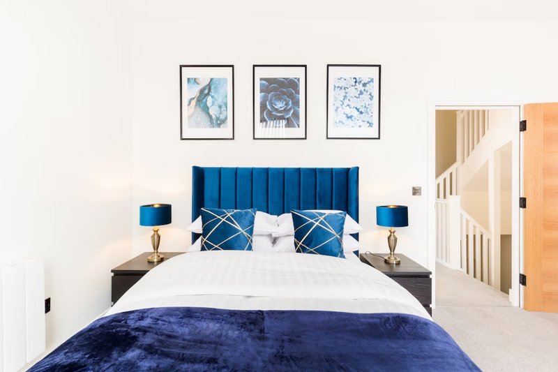 Modern bedroom with blue velvet headboard, white bedding, blue throw, framed artwork and wooden door