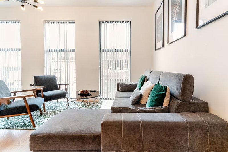 Modern living room with grey sofa, armchair, ottoman and vertical blinds