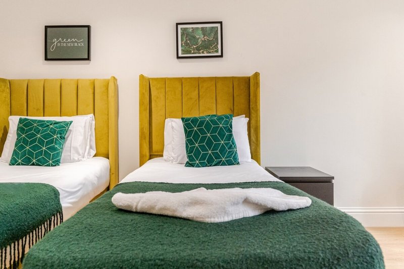 Bedroom with two single beds, yellow headboards, green bedding, and framed wall art