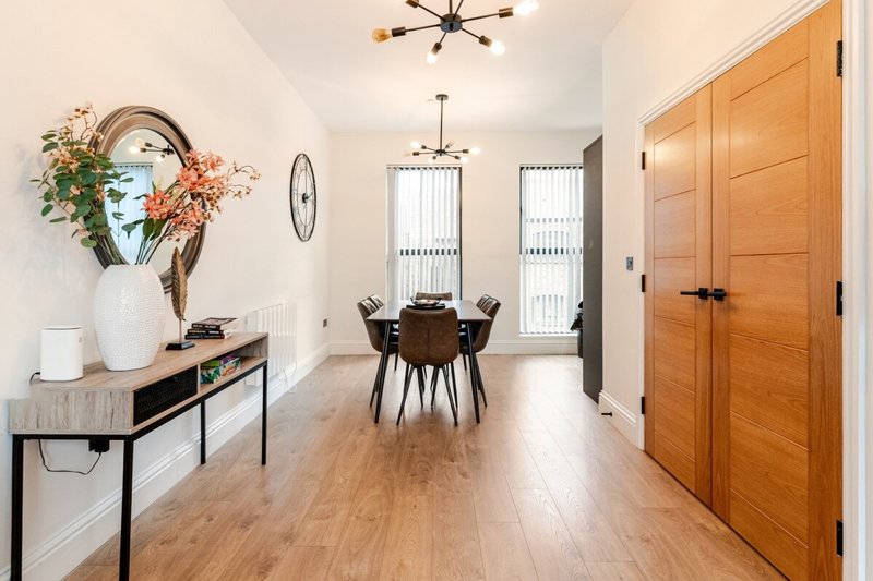 Open-plan hallway and dining area with wooden flooring, console table with flowers, and dining chairs