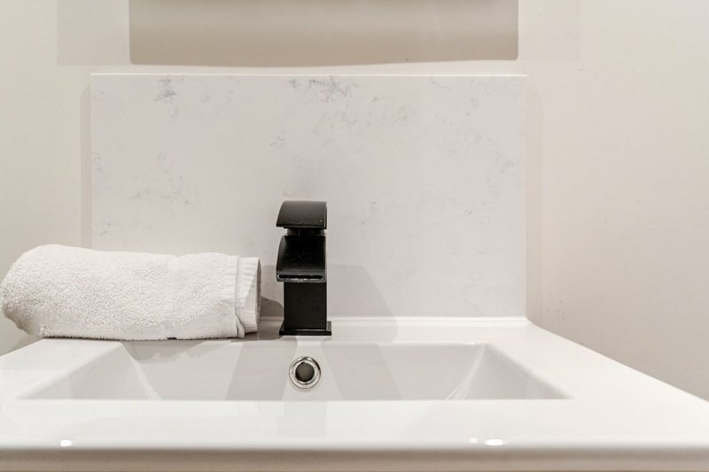 Modern bathroom sink with black tap, rolled white towel and backsplash