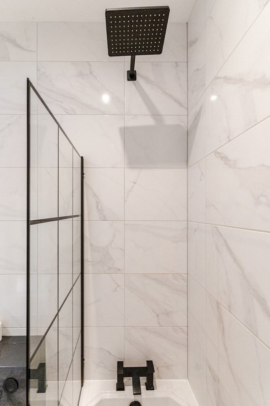 Modern bathroom shower with marble tiles, black rainfall showerhead, and glass partition
